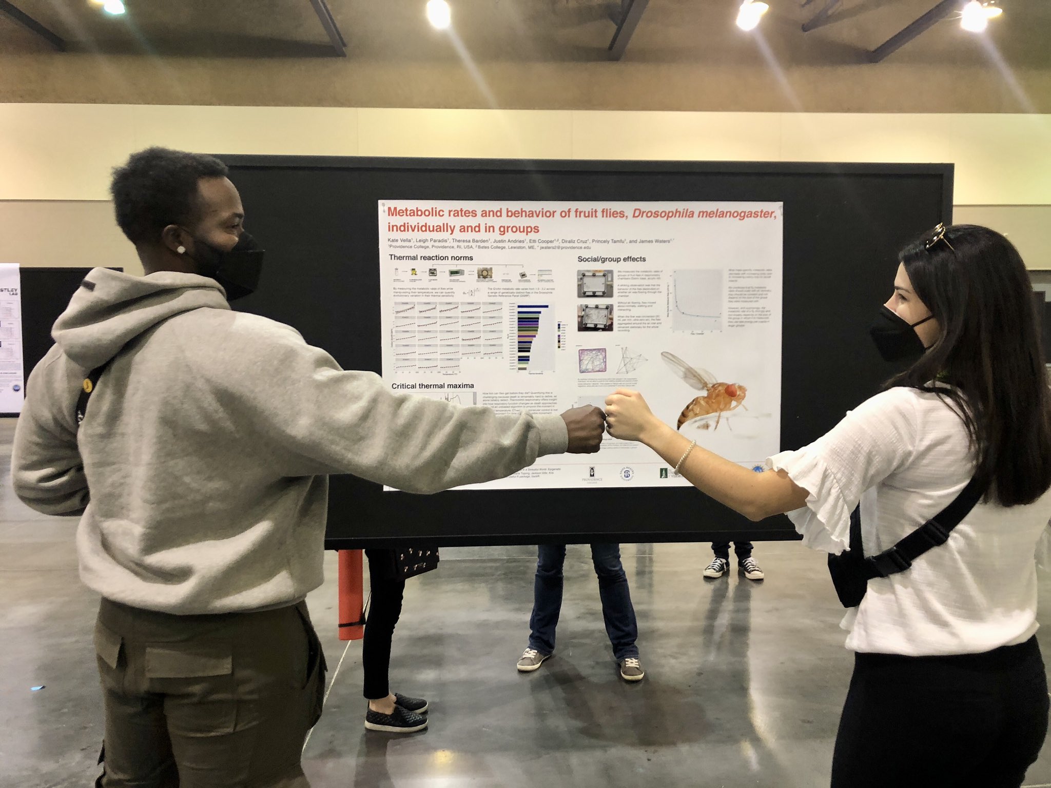 Two presenters fist bump in front of their poster at a scientific conference